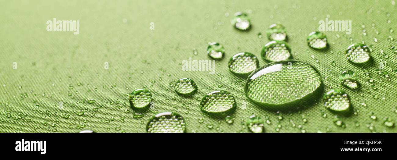 Fondo primer plano de gotas limpias redondas y pequeñas sobre tela impermeable verde protector húmedo impregnado con varias gotas de agua pequeñas Foto de stock