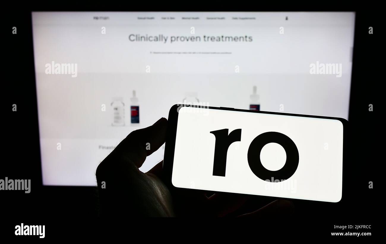 Persona que sostiene el teléfono celular con el logotipo de la empresa de telesalud Roman Health Ventures Inc. (RO) en la pantalla delante de la página web. Enfoque la pantalla del teléfono. Foto de stock