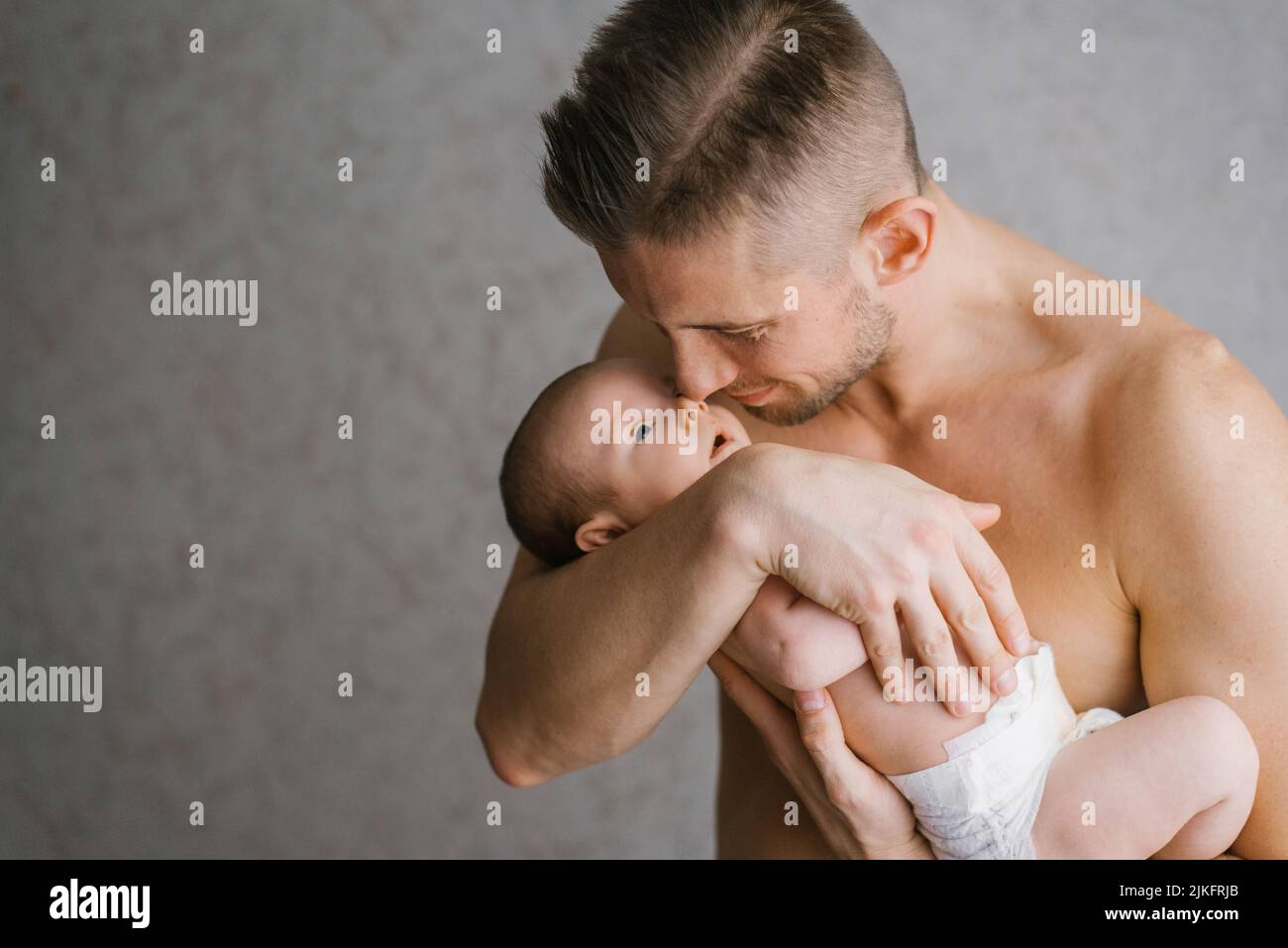 Un padre joven sostiene a su hijo recién nacido en un pañal en sus brazos Foto de stock