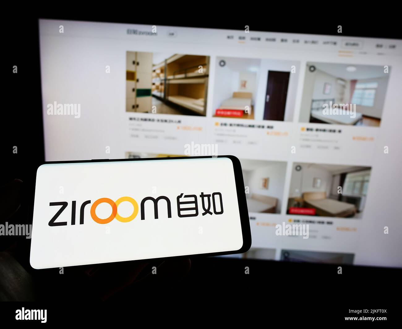 Persona que sostiene el teléfono celular con el logotipo de la compañía inmobiliaria china Ziroom en la pantalla delante de la página web del negocio. Enfoque la pantalla del teléfono. Foto de stock