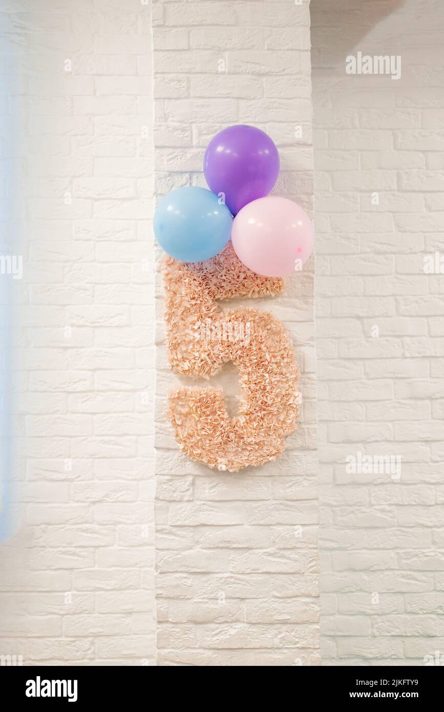 Rosa número 5 y globos cuelgan en una pared de ladrillo blanco. La decoración de la habitación de los niños para el cumpleaños del niño Foto de stock