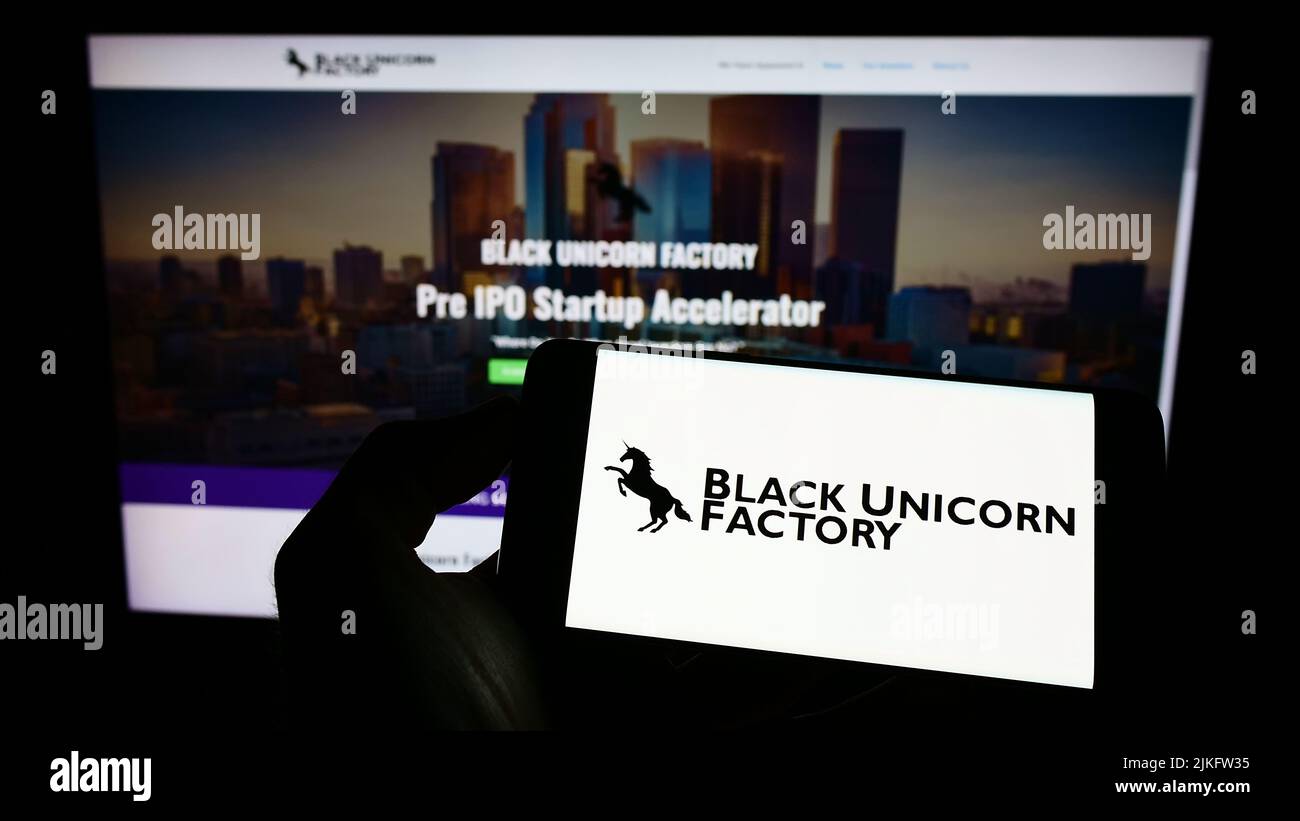 Persona que sostiene el teléfono celular con el logotipo de la compañía estadounidense de capital riesgo Black Unicorn Factory en la pantalla delante de la página web. Enfoque la pantalla del teléfono. Foto de stock