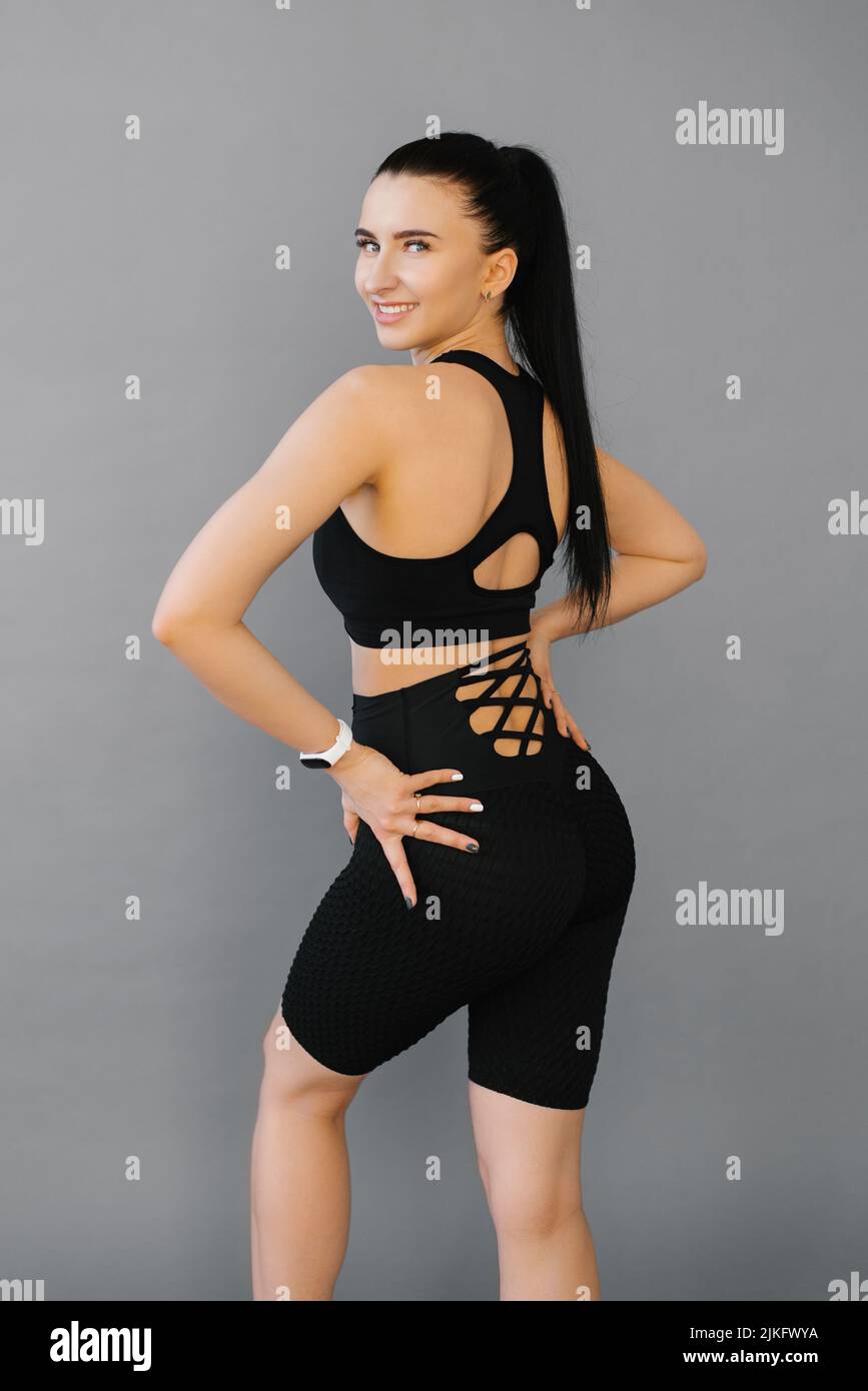Una mujer deportiva con una figura perfecta y nalgas en un traje negro sostiene sus manos por debajo de la cintura. Vista desde la parte de atrás Foto de stock