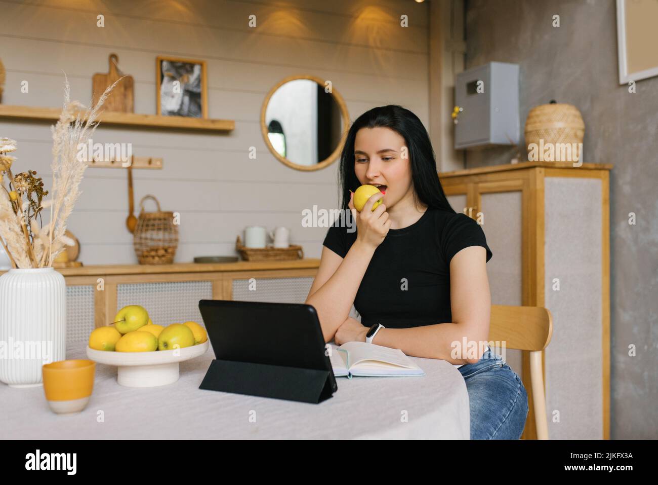 Una nutricionista o entrenadora de fitness está sentada en su escritorio frente a un ordenador portátil y hablando a través de un enlace de vídeo directo mientras se come un limón Foto de stock