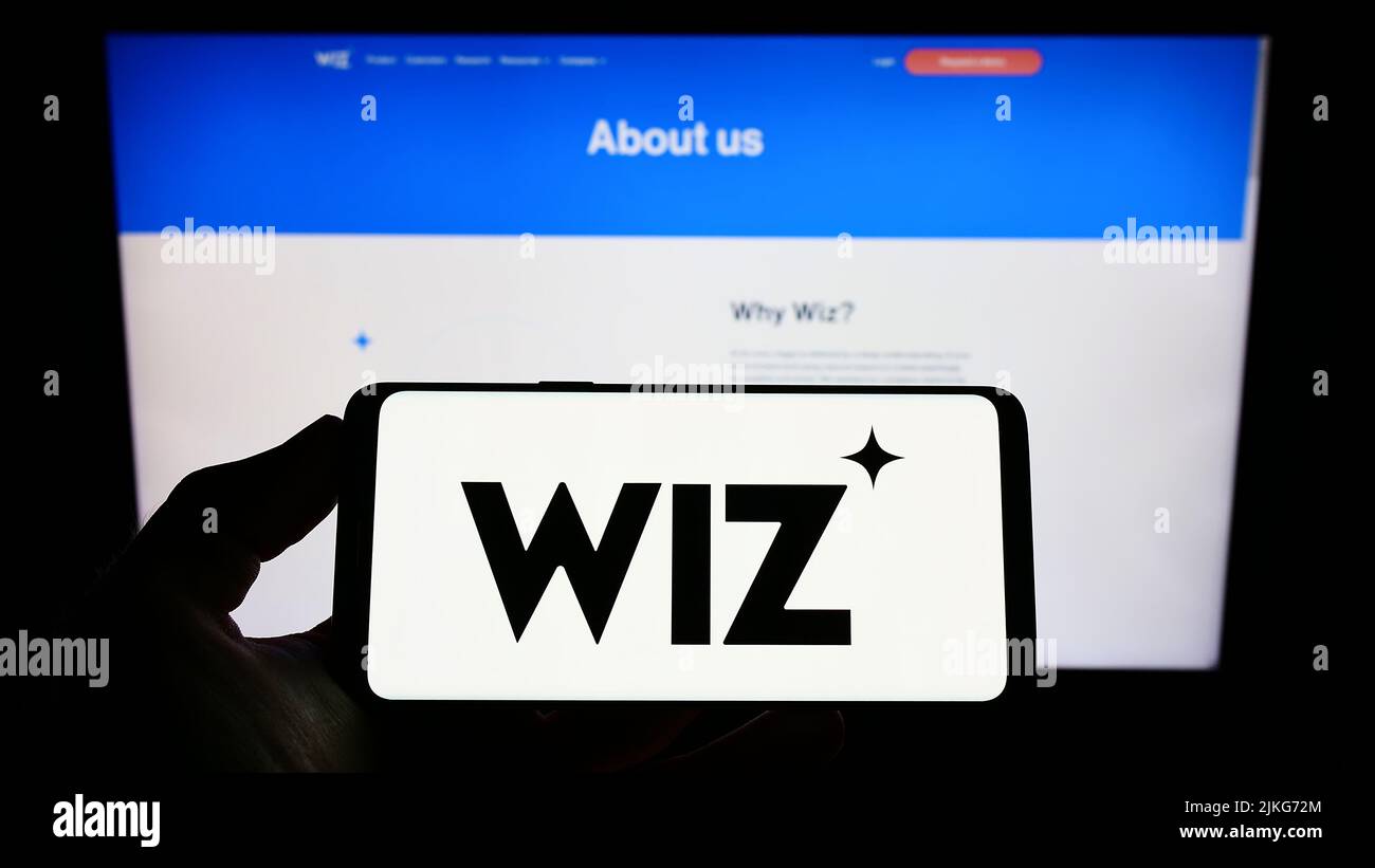 Persona con smartphone con el logotipo de la empresa estadounidense de seguridad en la nube Wiz Inc. En la pantalla delante del sitio web. Enfoque la pantalla del teléfono. Foto de stock