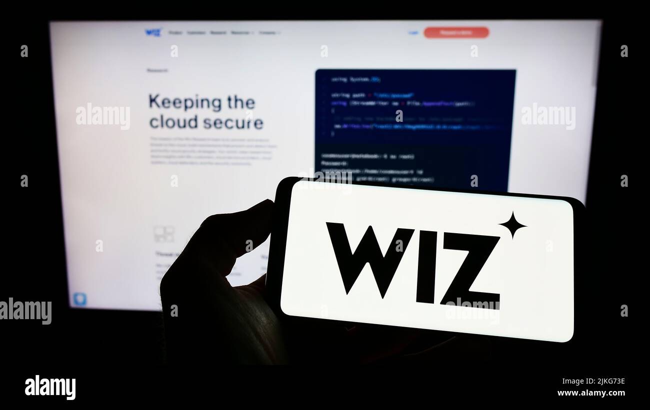 Persona que sostiene un teléfono móvil con el logotipo de la empresa estadounidense de seguridad en la nube Wiz Inc. En la pantalla delante de la página web. Enfoque la pantalla del teléfono. Foto de stock