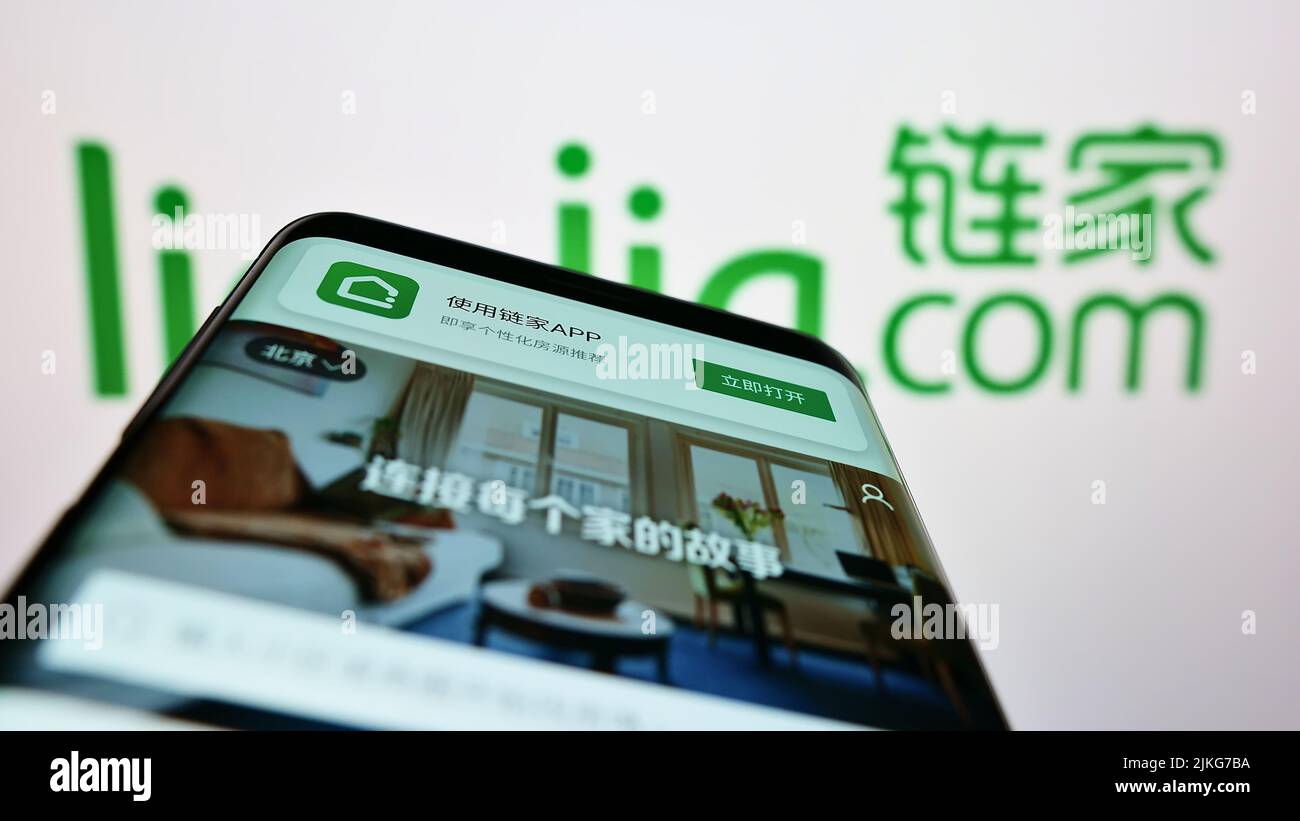 Teléfono móvil con sitio web de la empresa inmobiliaria china Lianjia en pantalla delante del logotipo del negocio. Enfoque en la parte superior izquierda de la pantalla del teléfono. Foto de stock