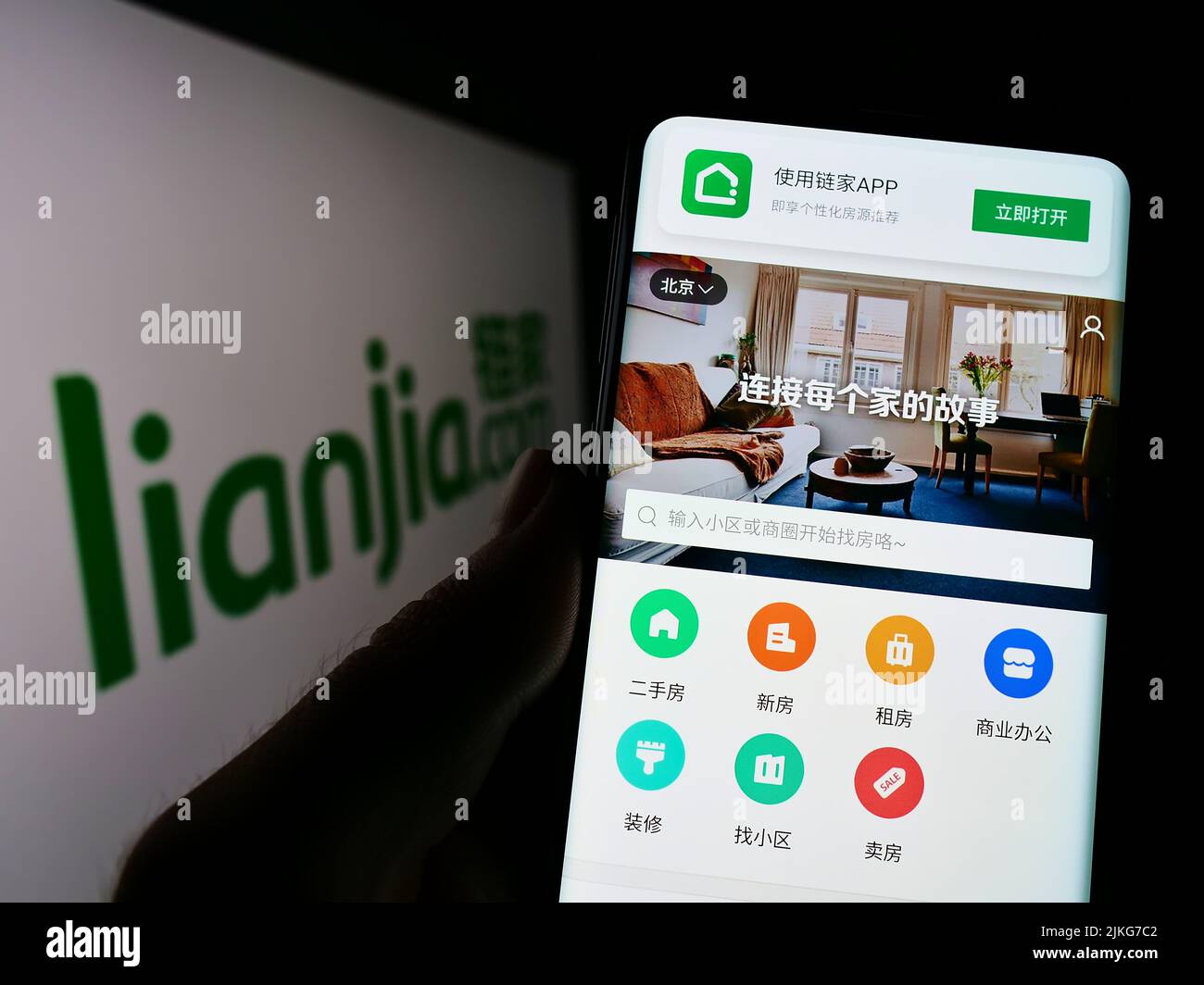 Persona que sostiene smartphone con la página web de la compañía inmobiliaria china Lianjia en la pantalla delante del logotipo. Enfoque en el centro de la pantalla del teléfono. Foto de stock