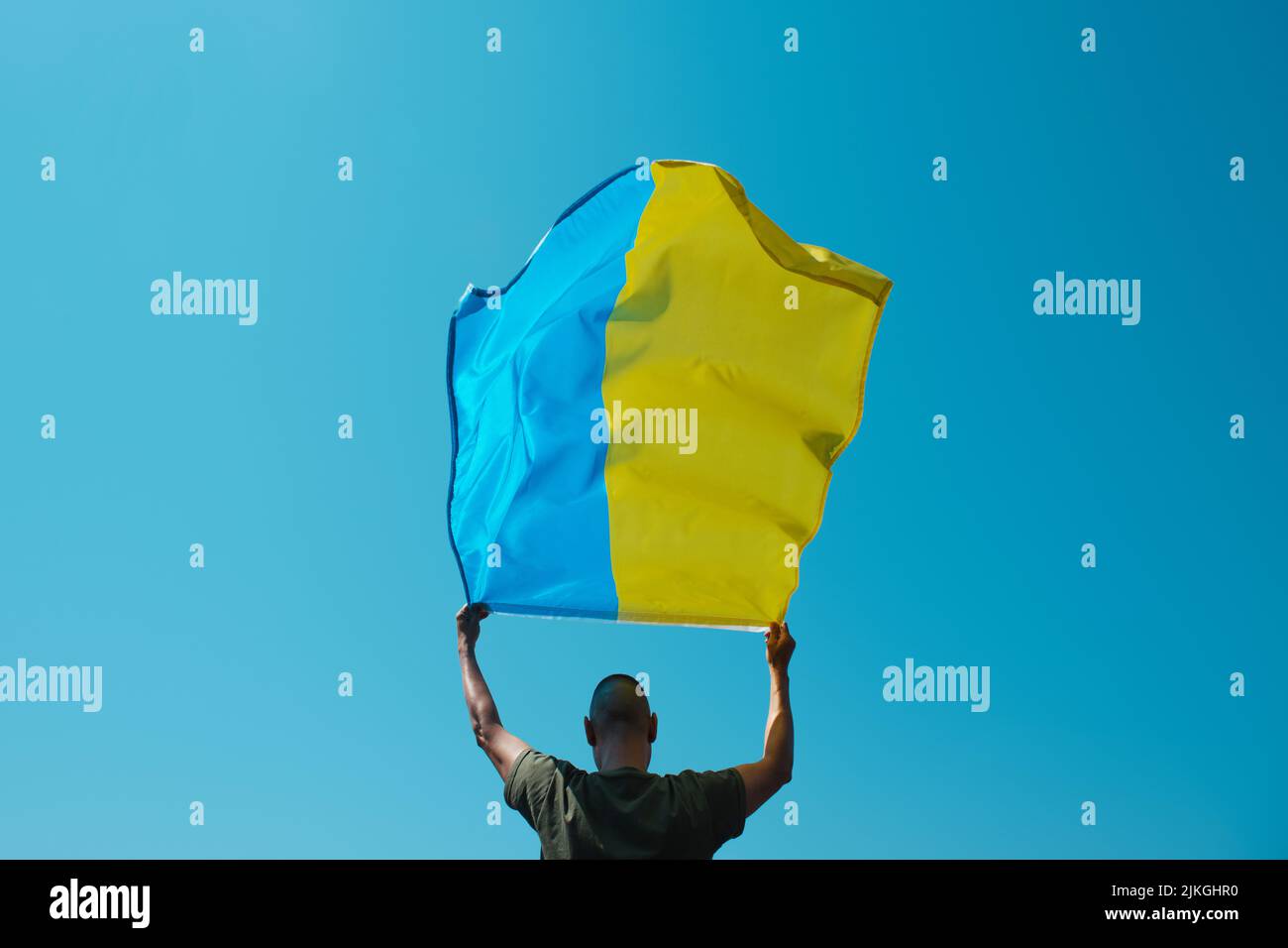 un hombre, visto desde atrás, ondea la bandera ucraniana sobre su cabeza en el cielo en un día soleado Foto de stock