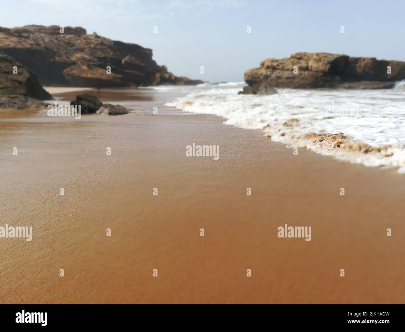 Un primer plano de las olas del mar en la playa de arena con piedras en Marruecos Foto de stock