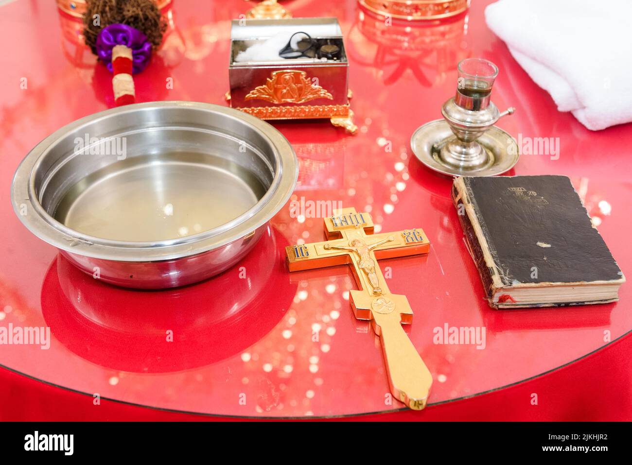Una cruz dorada, la biblia, un tazón de agua santa, y un ataúd sobre una mesa roja de la iglesia - ceremonia de bautismo Foto de stock