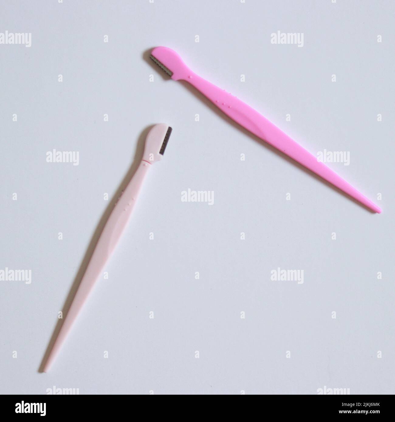 Una cara y cejas dos afeitadoras rosadas sobre una superficie blanca Foto de stock
