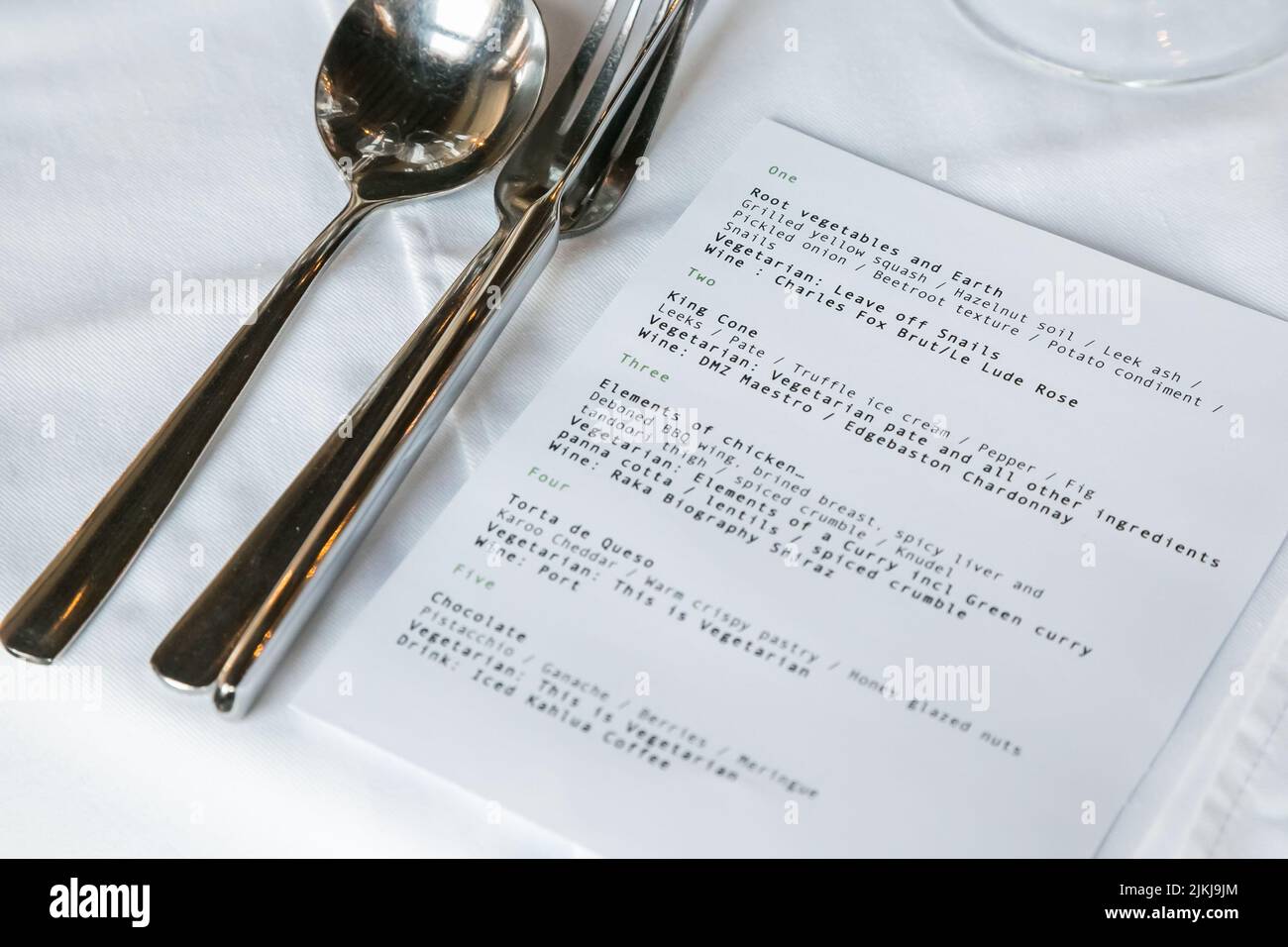 Un primer plano de un menú y cubiertos en una mesa de restaurante con cubierta de tela blanca Foto de stock