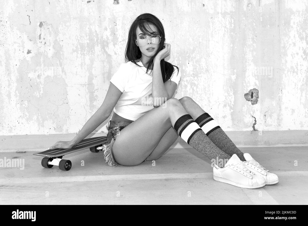Sexy caucásica joven urbana con longboard sentado en la calle blanco y negro Foto de stock