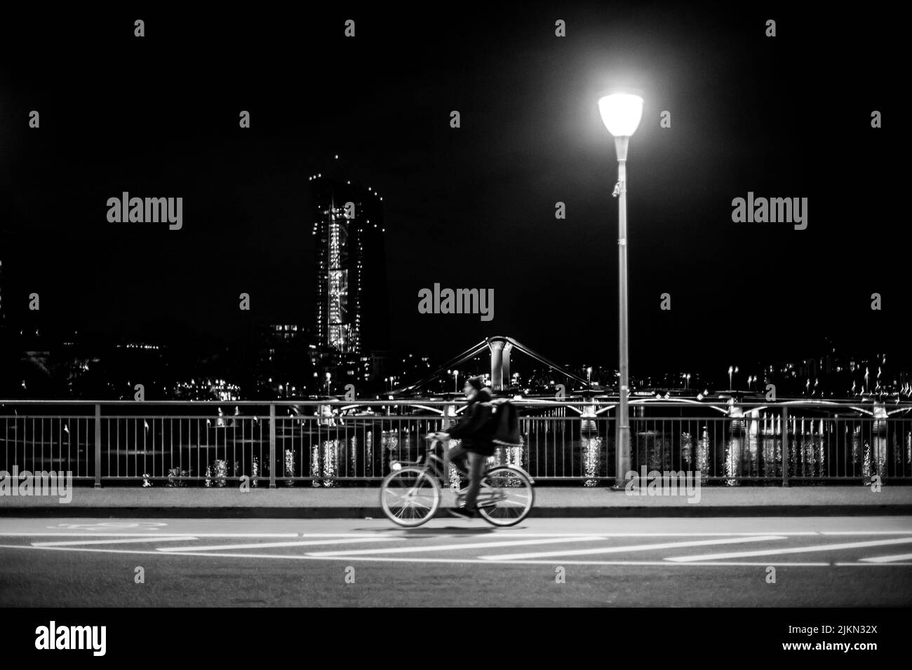 El ciclista montando a lo largo del puente por la noche con la ciudad al fondo. Foto de stock