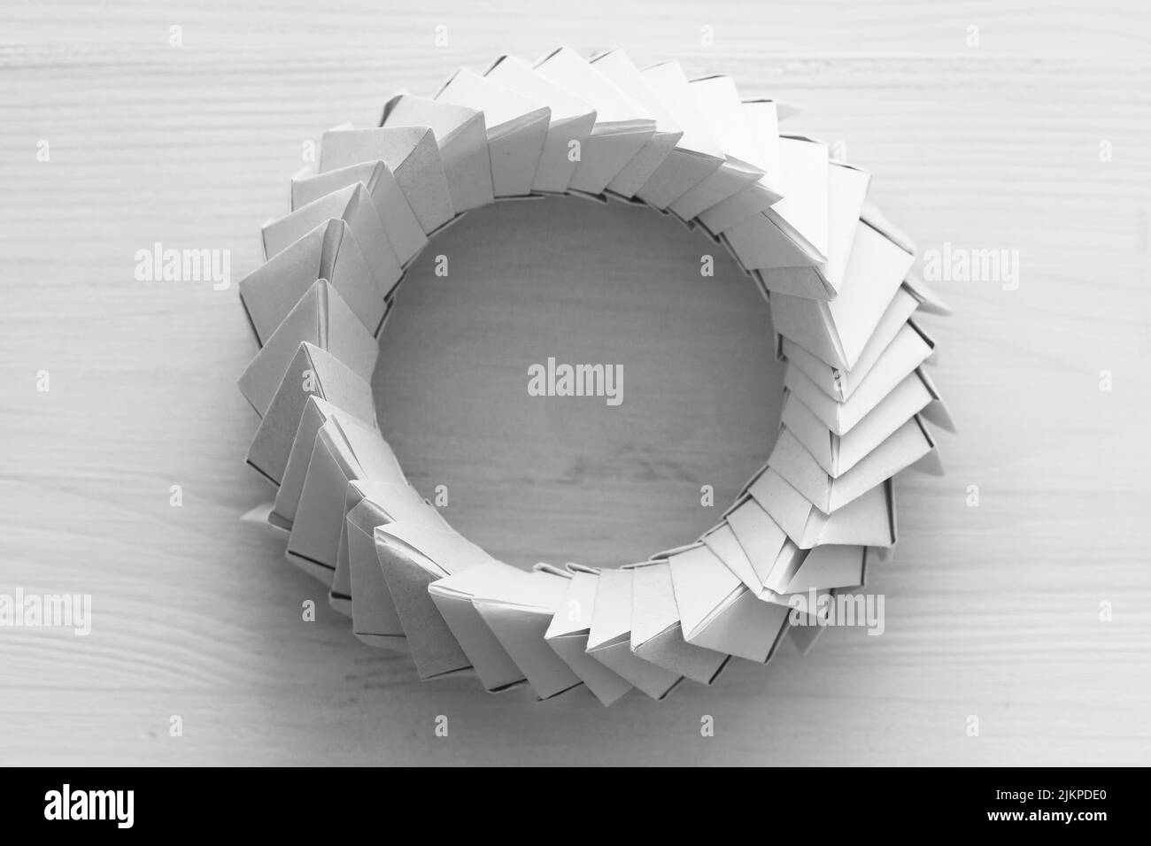 Anillo de origami. Objeto paramétrico abstracto hecho de hojas de papel enlazadas en mesa blanca, vista superior Foto de stock