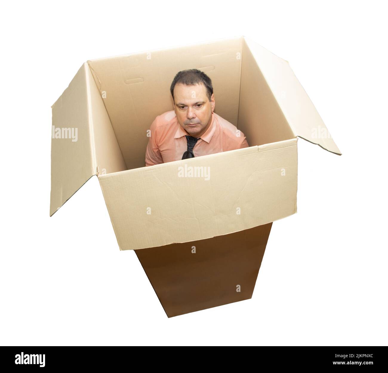 Un hombre sudoroso en una camisa con corbata se coloca dentro de una caja de cartón, aislado sobre fondo blanco Foto de stock