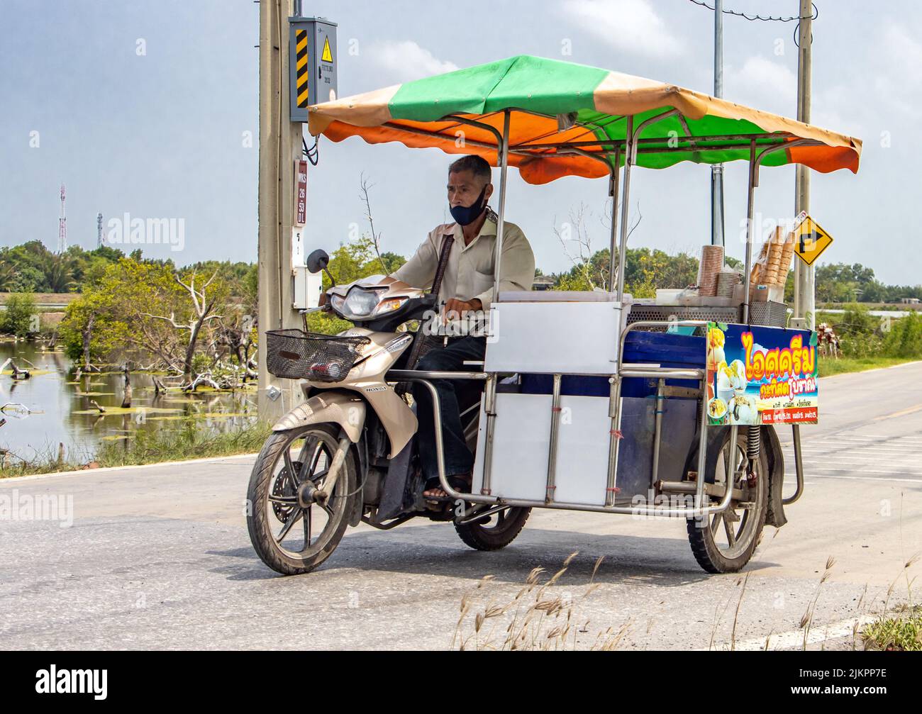 SAMUT PRAKAN, TAILANDIA, 01 2022 DE JUNIO, un vendedor de helados monta una motocicleta de tres ruedas a lo largo de una carretera de la aldea Foto de stock