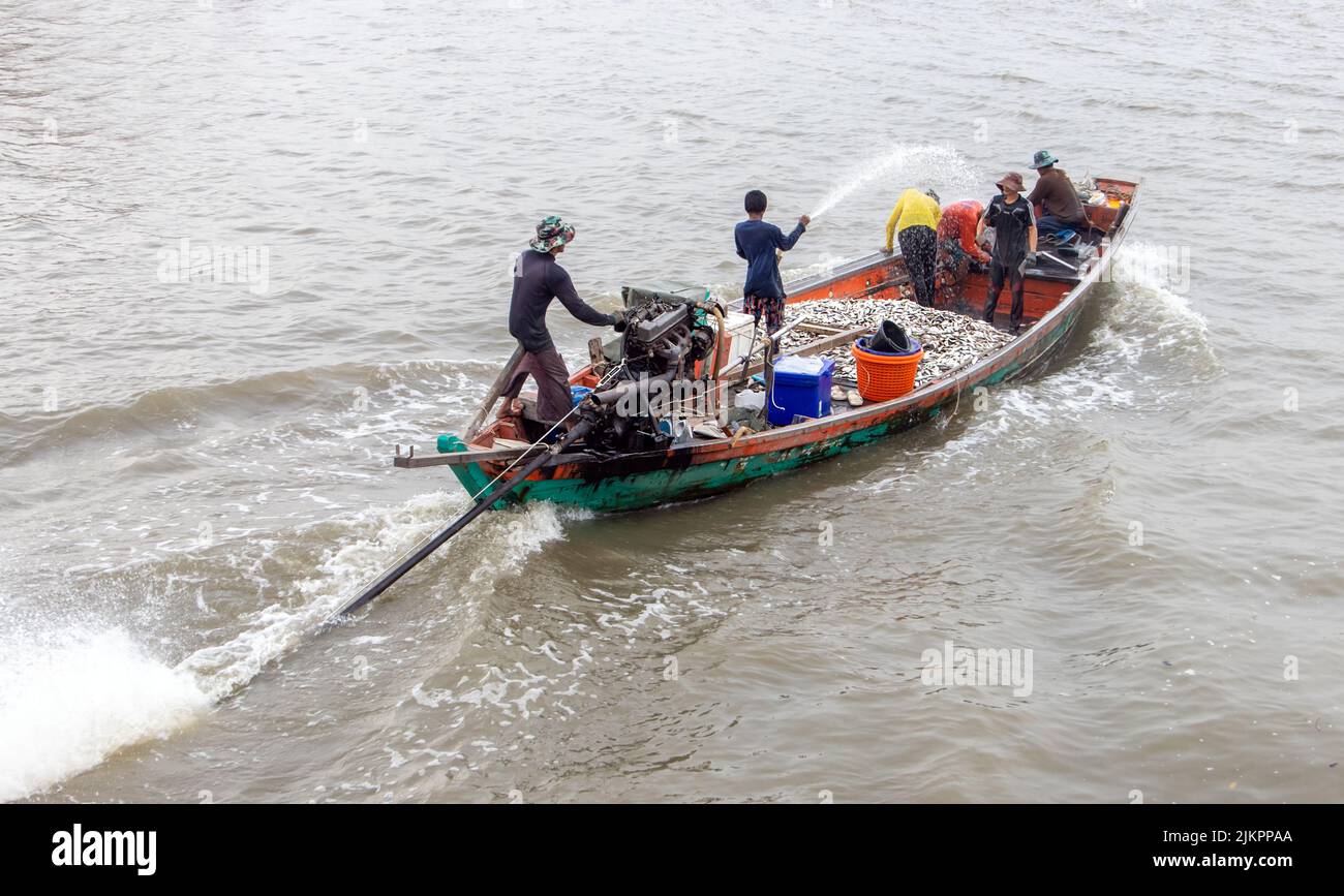 Los pescadores asiáticos navegan en un barco lleno de peces capturados Foto de stock