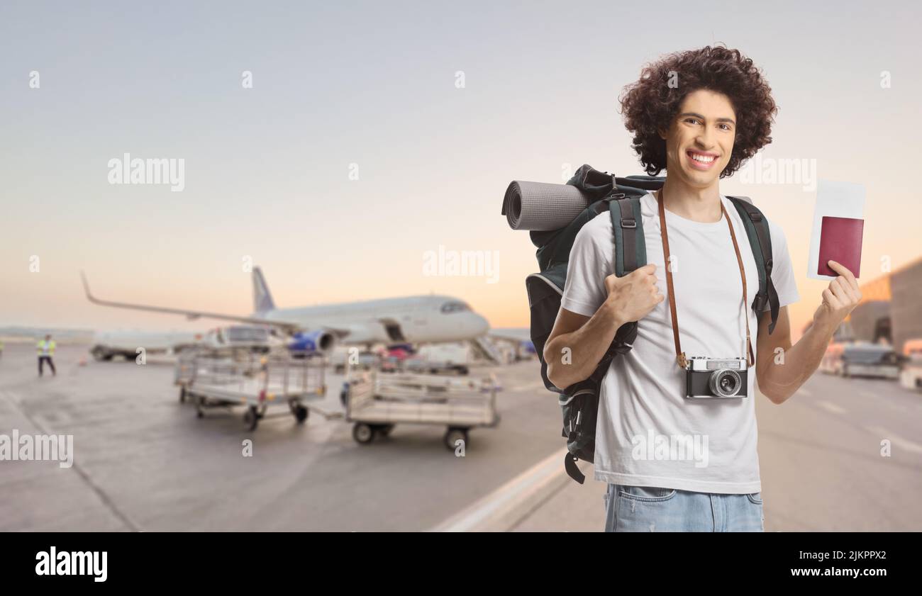 Joven turista masculino con una mochila mostrando un pasaporte y sonriendo en un delantal del aeropuerto Foto de stock