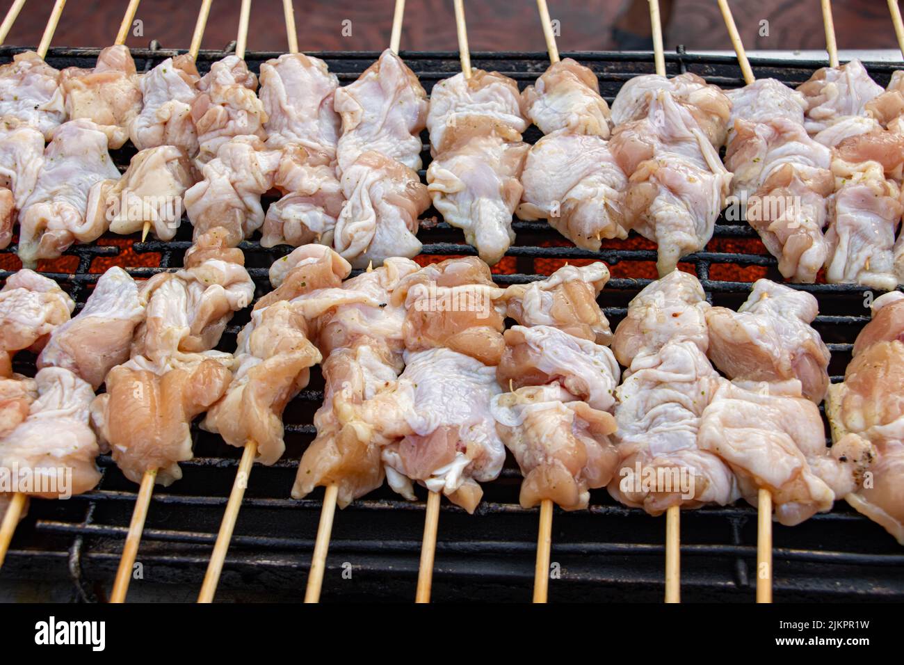 La carne cruda en un palo se asa en la parrilla. Preparación de pollo en un palo en un mercado tailandés Foto de stock
