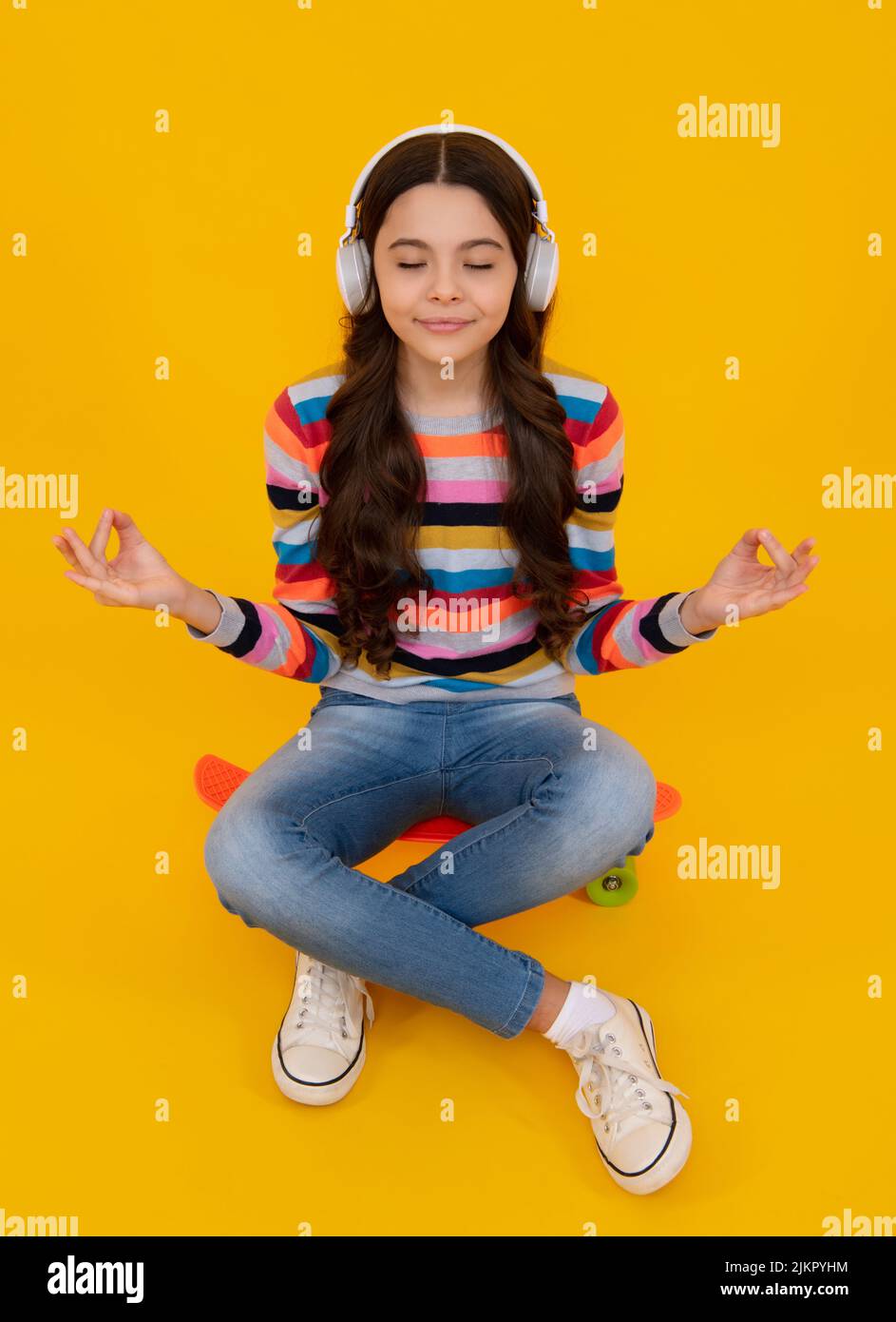 Niña adolescente con auriculares escuchando música, llevando un conjunto elegante y casual aislado sobre fondo amarillo. Foto de stock