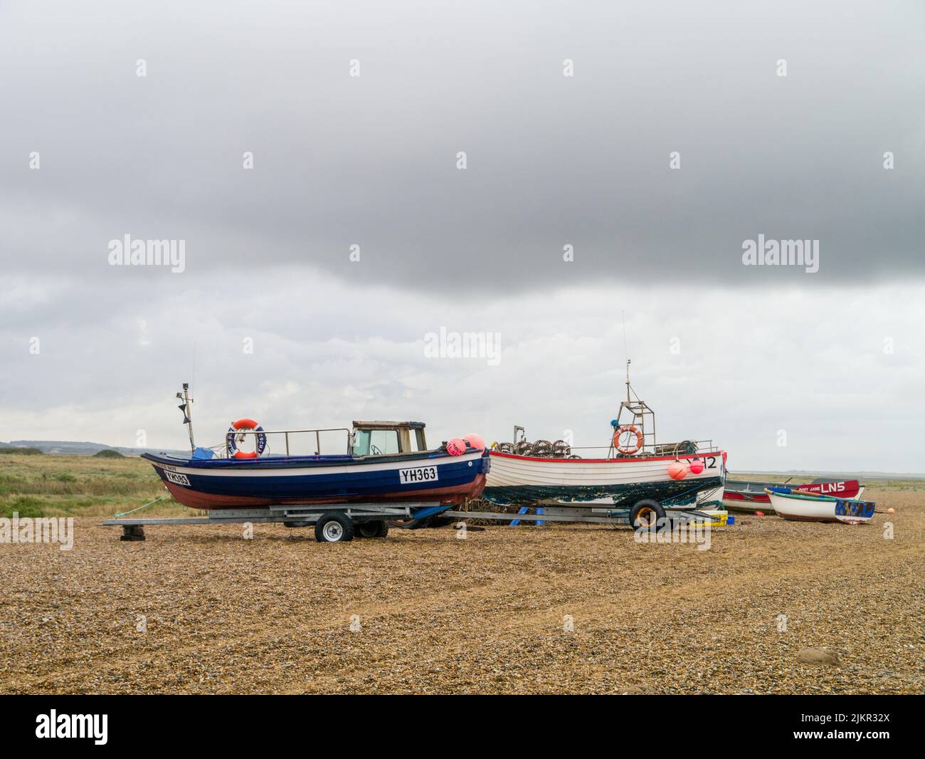 Barcos de pesca bajo un cielo malhumorado en la playa de guijarros del complejo de Cley, North Norfolk, Reino Unido Foto de stock