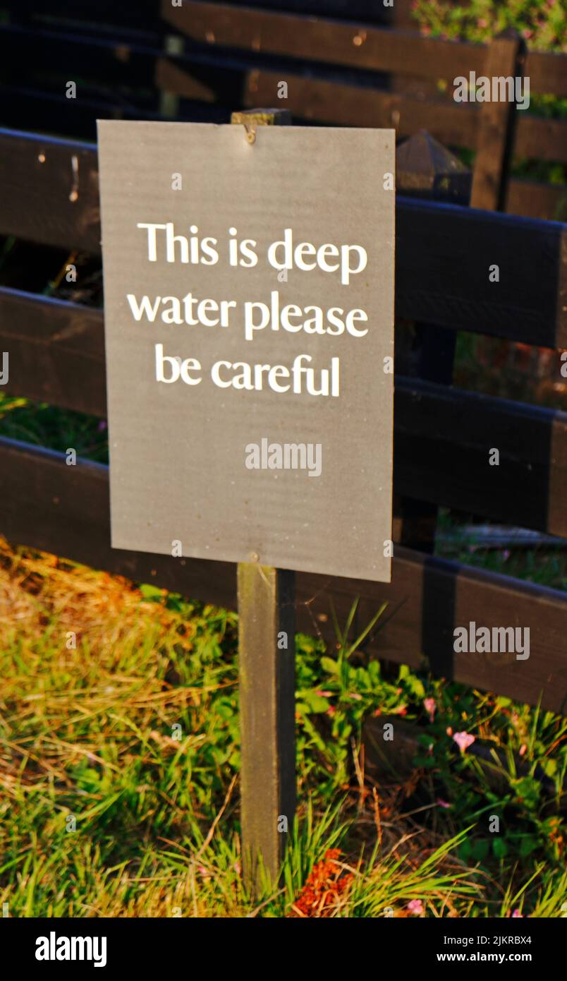 Una señal de advertencia de aguas profundas por el molino de viento restaurado en los Norfolk Broads en Horsey, Norfolk, Inglaterra, Reino Unido. Foto de stock