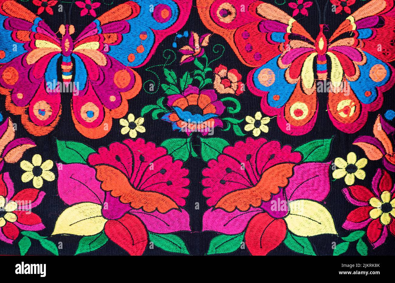 Telas coloridas y artesanales de Chiapas, México. Flores bordeadas en varios colores y mariposas sobre fondo negro Foto de stock