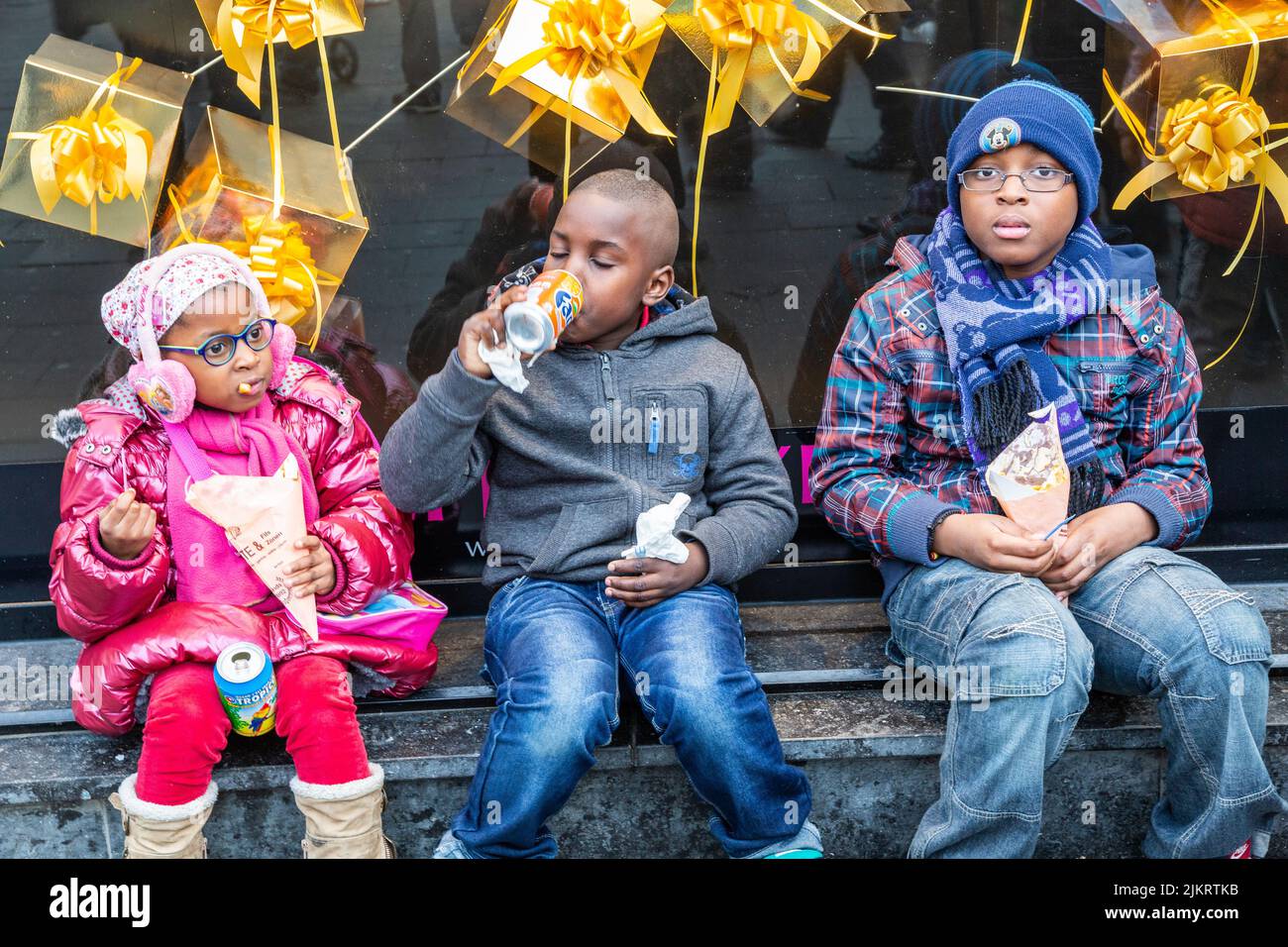 Tres niños africanos sentados degustando especialidades belgas. Foto de stock