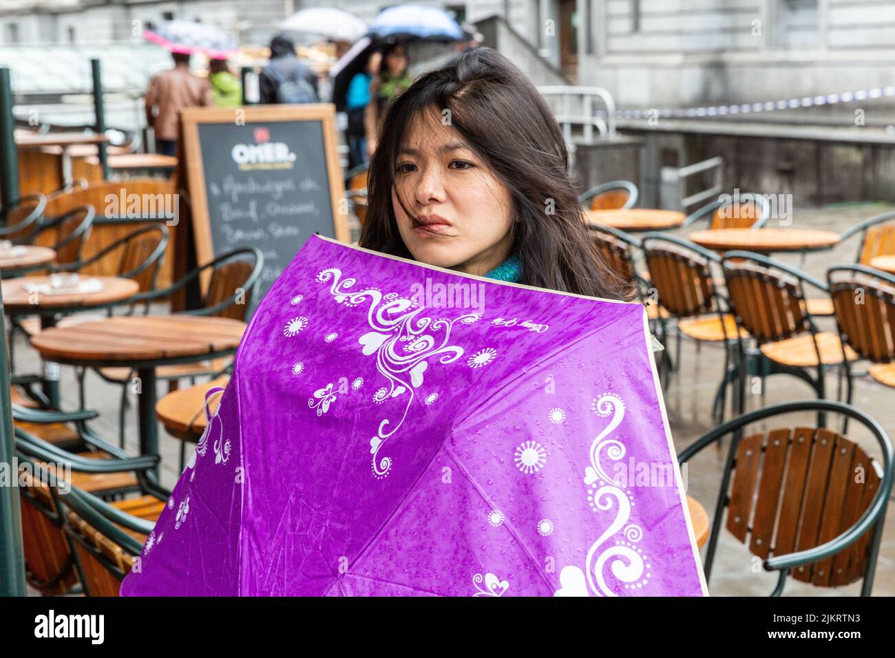 Joven asiática abriendo su paraguas púrpura en un día lluvioso en una calle de Bruselas. Foto de stock
