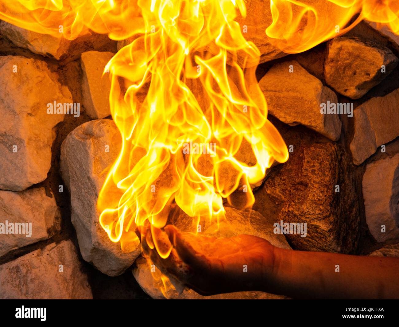 Un primer plano de las llamas de fuego sobre la mano del hombre que se sostiene cerca de la pared de ladrillo Foto de stock