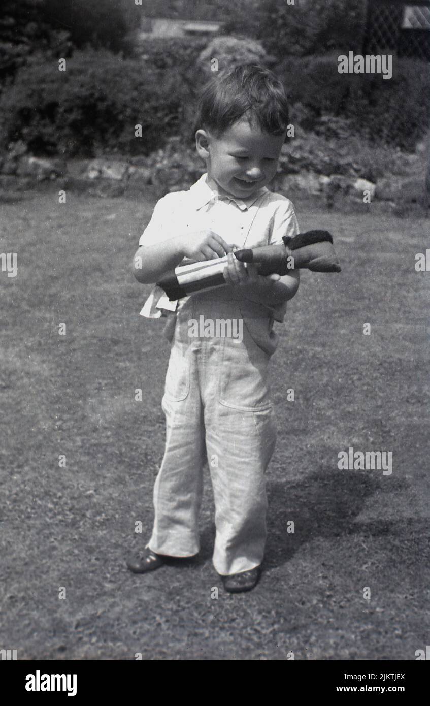 1967, histórico, fuera en el jardín, un niño feliz de pie en la hierba sosteniendo su juguete suave, un golly, Inglaterra, Reino Unido. Foto de stock