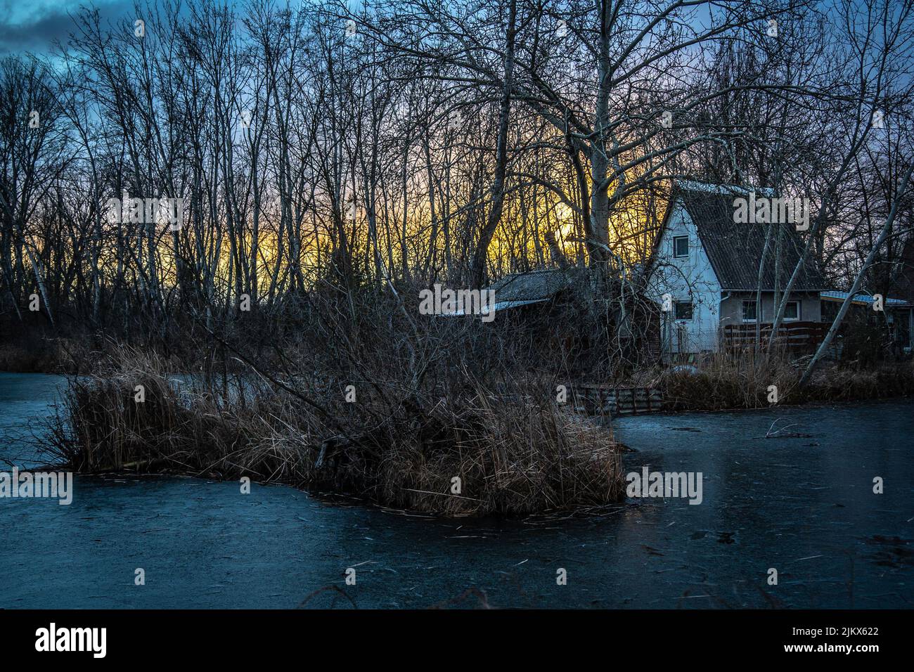 Dunakeszi, Hungría - 30 2022 de enero: Puesta de sol colorida con cañas y lago congelado, y una casa que parece estar encantada Foto de stock