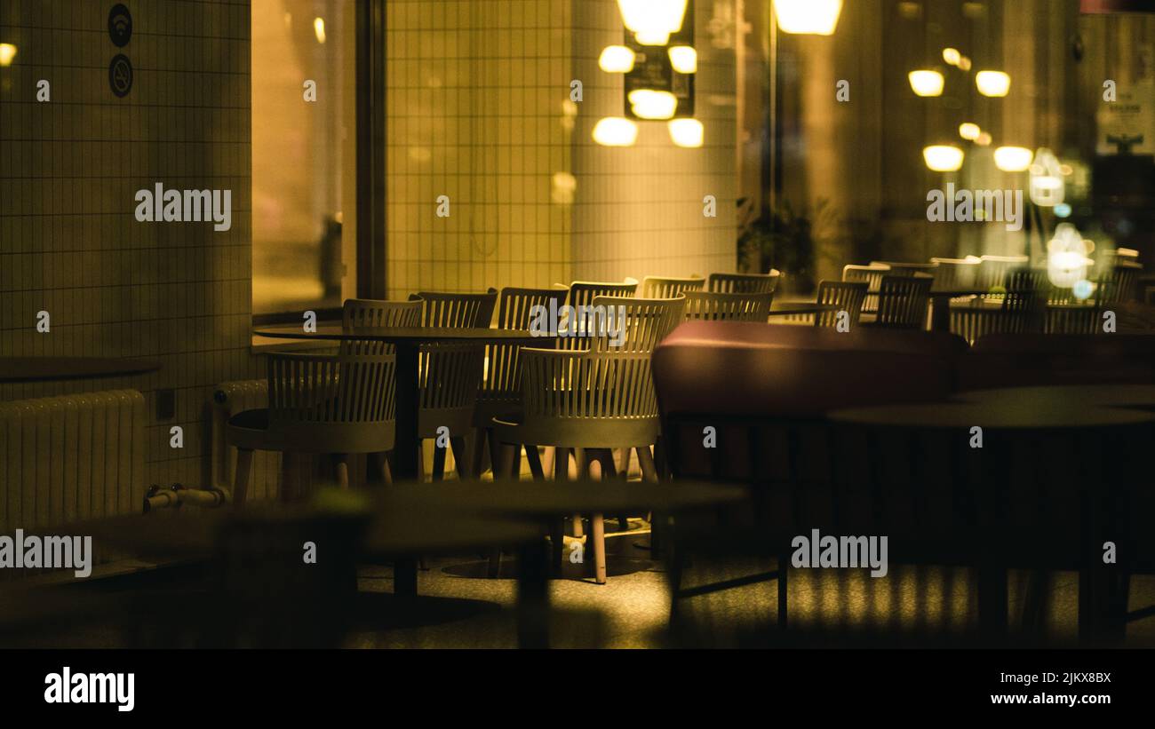Una foto hermosa de un café sillas y mesas vacías iluminadas por bombillas amarillas Foto de stock