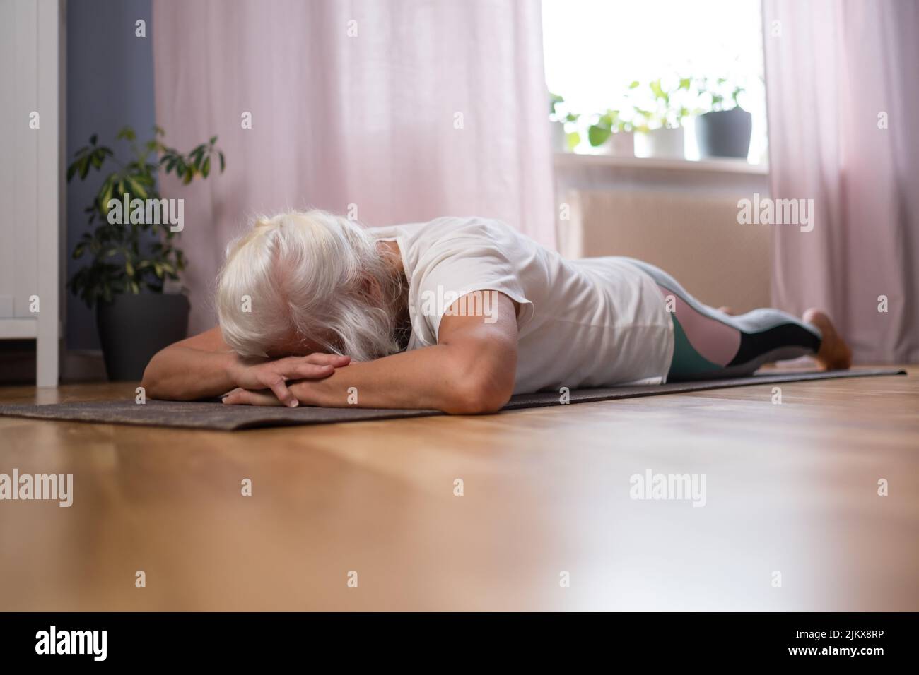Mujer mayor acostada en una colchoneta de yoga y relajante mientras disfruta del yoga en casa Foto de stock