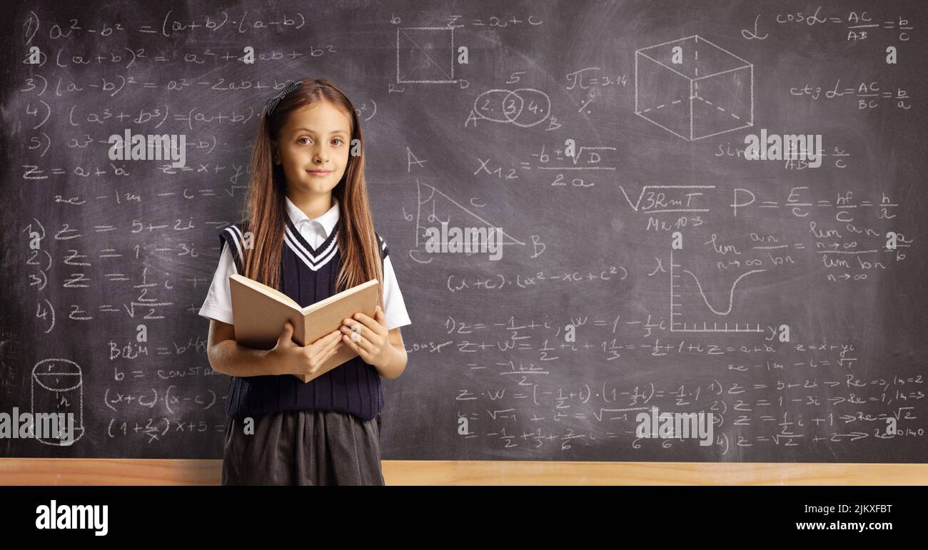 Alumna con un libro delante de una pizarra con geometría y fórmulas matemáticas Foto de stock