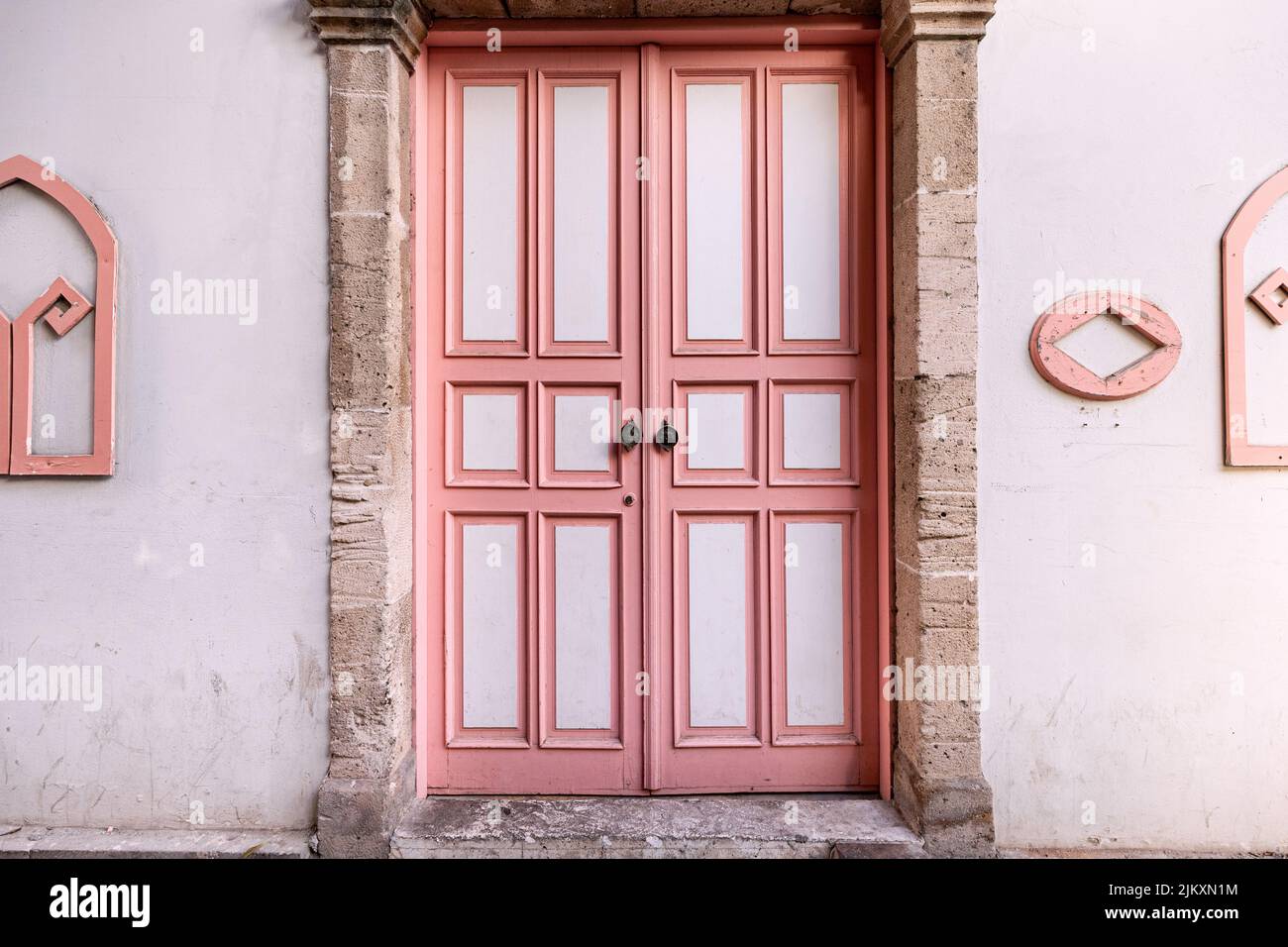 puerta de madera de época pintada de blanco y rosa en el casco antiguo de la ciudad. Foto de stock