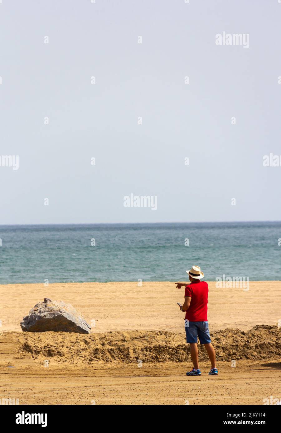 hombre de espalda con sombrero en la playa señalando Foto de stock