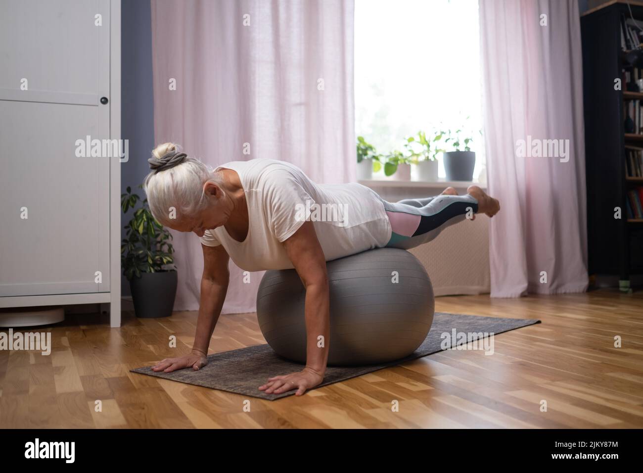 Entrenamiento en casa. Mujer mayor deportiva haciendo una tabla de yoga con una pelota haciendo ejercicio en la sala de estar Foto de stock