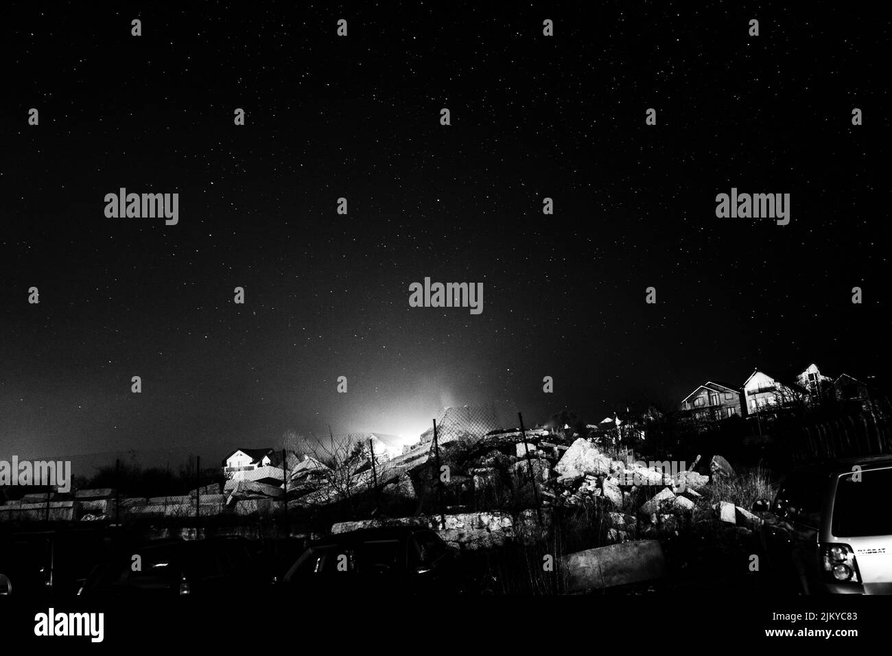 Una imagen en escala de grises de un cielo nocturno estrellado en un campo sobre una pequeña casa y un coche aparcado en el lateral Foto de stock