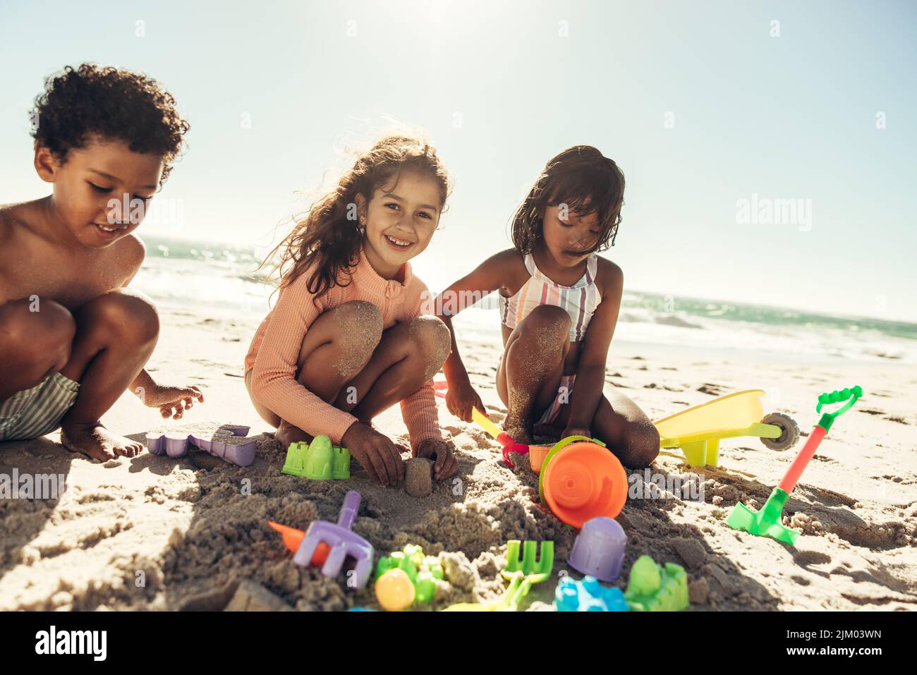 Grupo de niños felices jugando con sus juguetes en la arena de la playa. Tres niños despreocupados pasando un buen rato en una playa soleada durante las vacaciones de verano. Foto de stock