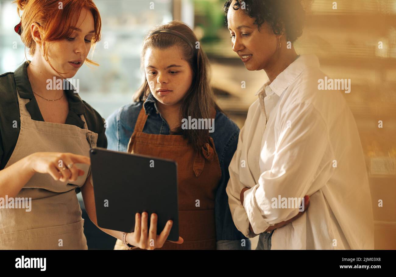 Gerente de supermercado usando una tableta digital mientras mantiene una conversación con sus empleados en una reunión de personal. Grupo de diversas mujeres trabajando juntas Foto de stock