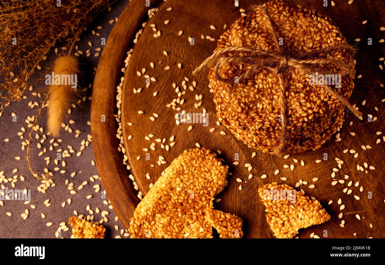 Galletas de sésamo atadas con una cuerda sobre una tabla de madera con semillas de sésamo en el fondo Foto de stock