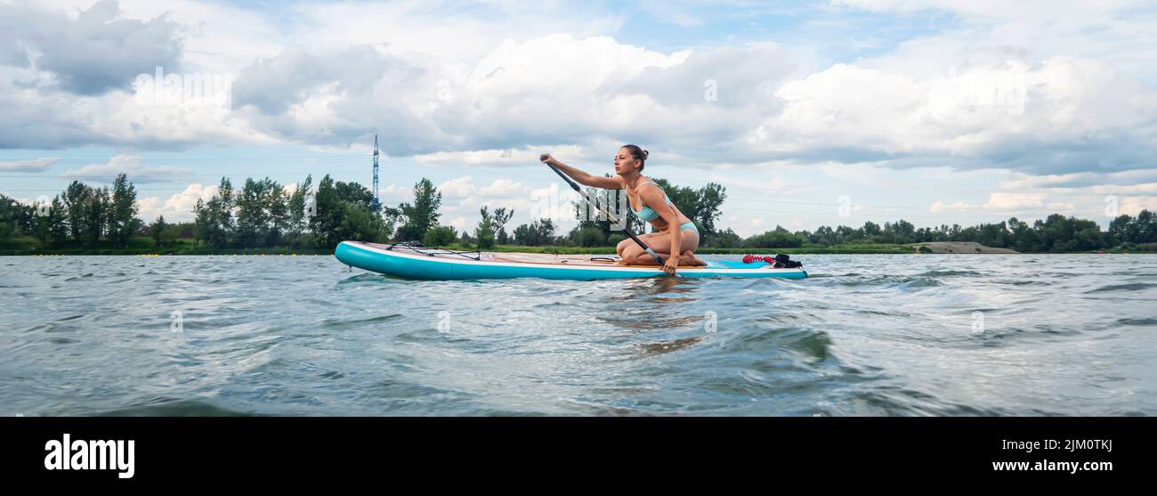 La mujer caucásica está montando una tabla de SUP en el río en la ciudad. Deportes de verano. panorama Foto de stock