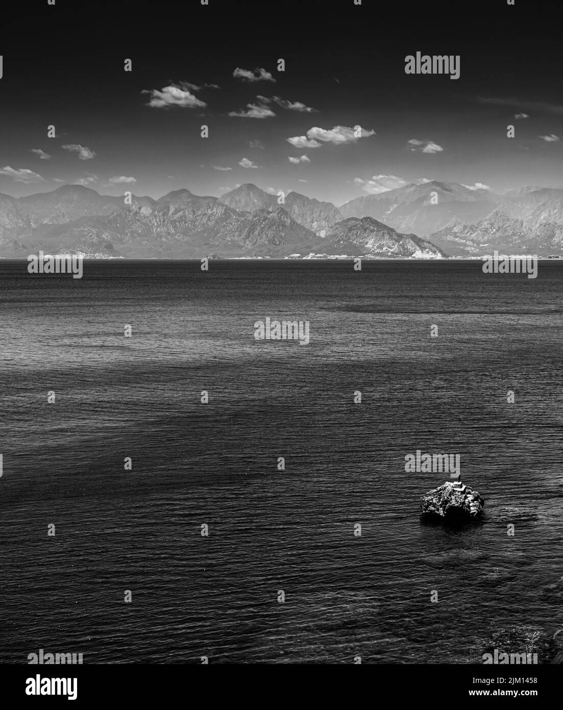 Blanco y negro BW Moody y fotografía atmosférica de un paisaje marino con montañas y roca solitaria Foto de stock