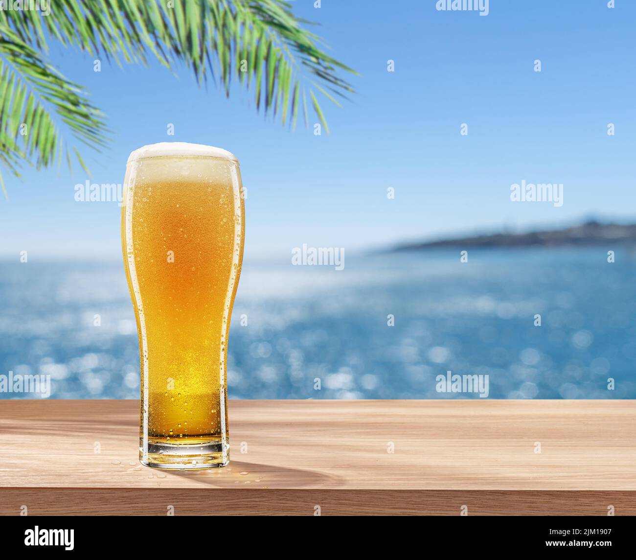 Vaso de cerveza fría sobre la mesa y un mar borroso y brillante al fondo. Lugar para mostrar su nombre de producto o marca. Foto de stock
