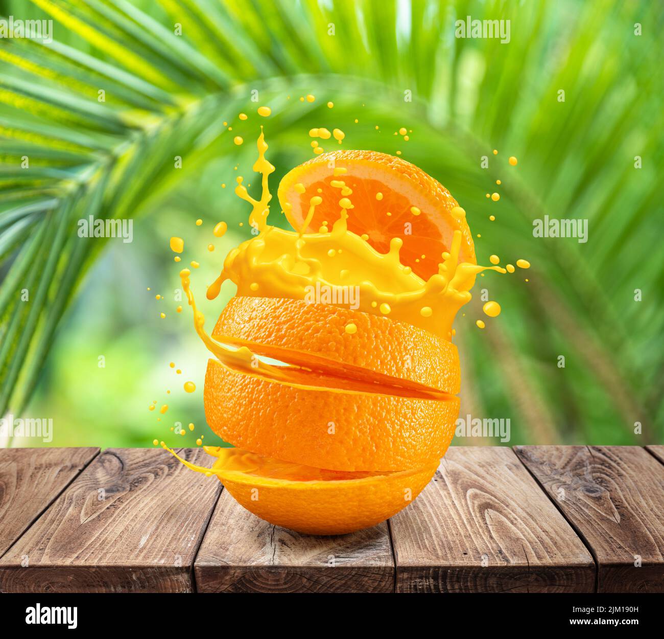 Rodajas de fruta naranja salpicando zumo de naranja sobre la mesa de madera. Hojas verdes de palma en el fondo. Foto de stock
