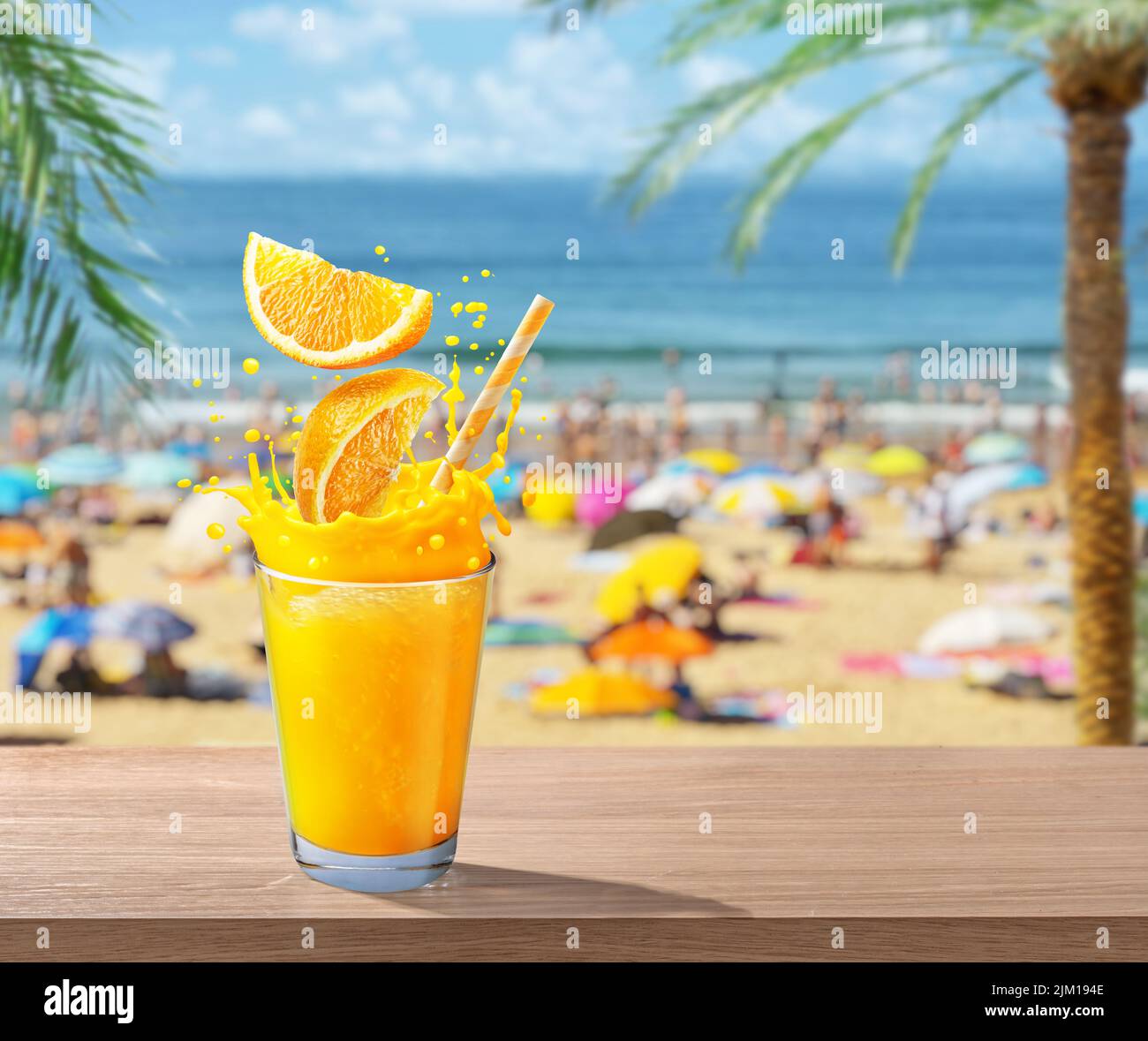 Vaso de zumo de naranja con chapoteo. Foto borrosa de playa abarrotada al fondo. Concepto de vacaciones de verano. Foto de stock