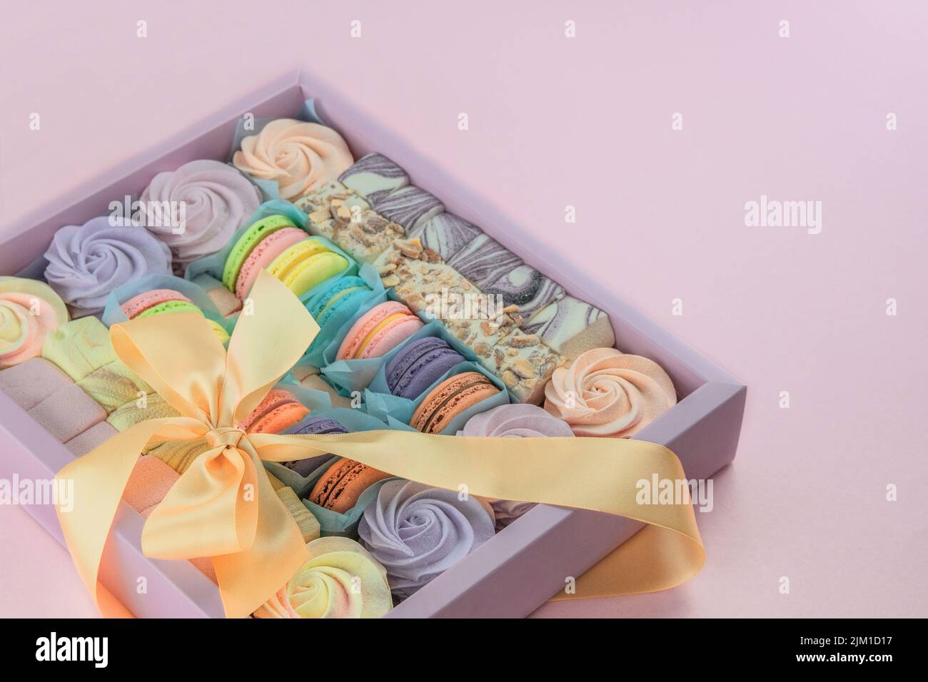Macaroons y malvaviscos en caja en fondo rosado, primer plano. Tradicionales postres dulces de colores para el presente para las vacaciones. Foto de stock